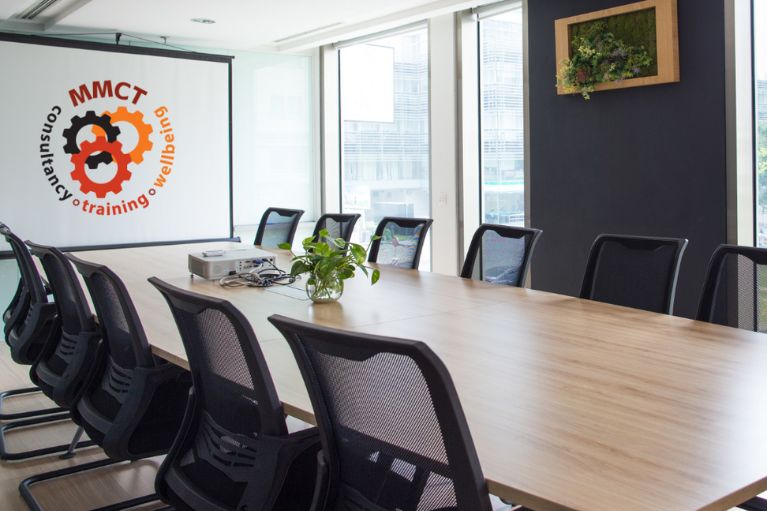 Train the Trainer Training course room illustrating a board room with a long table, 11 chairs and a whiteboard with the MMCT logo displayed upon it